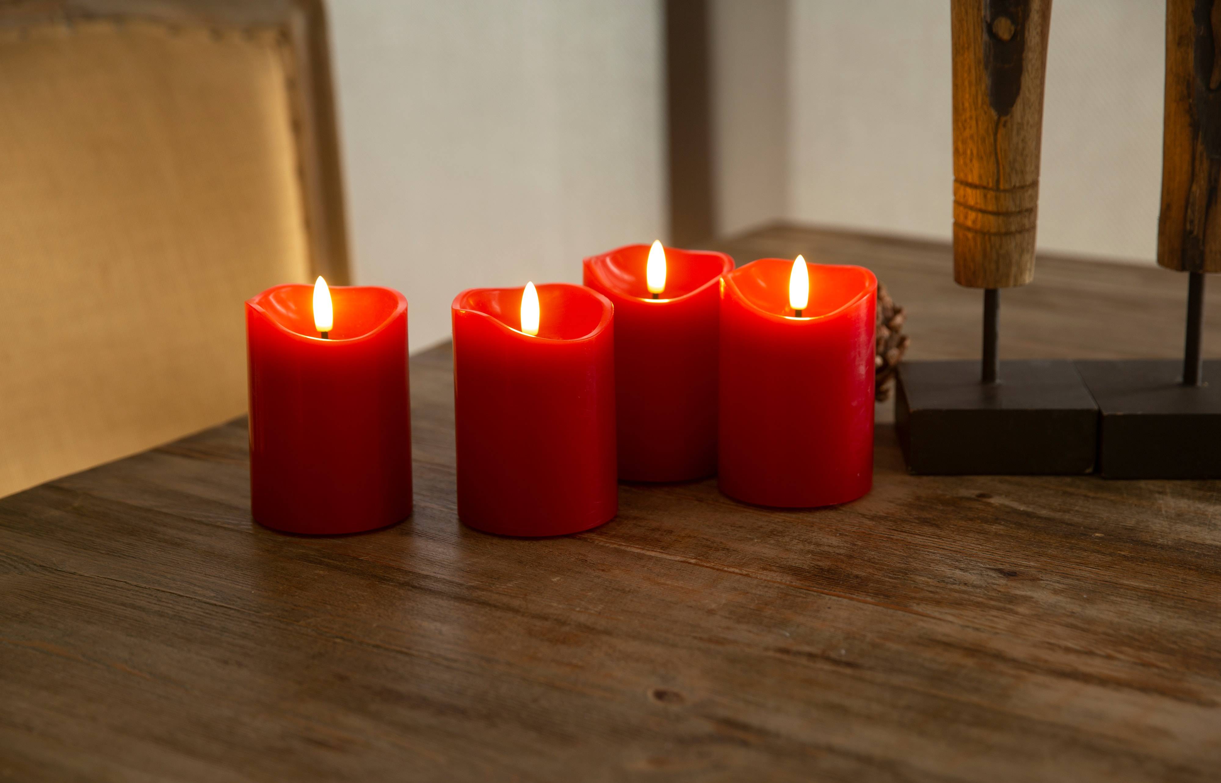 Vier brennende rote Kerzen auf einem Holztisch, die eine warme, beruhigende Atmosphäre schaffen.