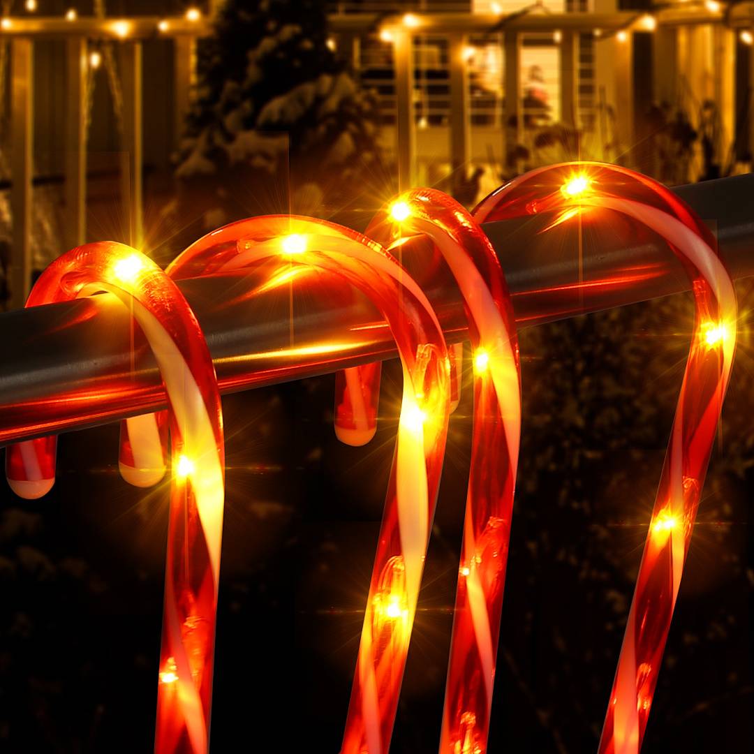 Leuchtende rot-weiße Zuckerstangen-Lichter, die nachts um ein Metallgeländer gewickelt sind, mit einem warm beleuchteten Gebäude im Hintergrund.
