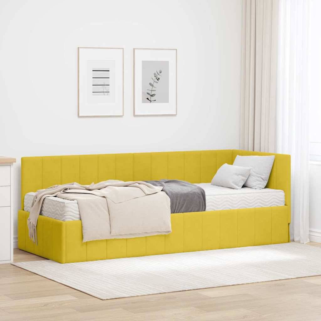 Ein gelbes gepolstertes Tagesbett mit grauen und beigen Kissen und einer beigen Decke steht an einer weißen Wand mit gerahmter Kunst darüber.