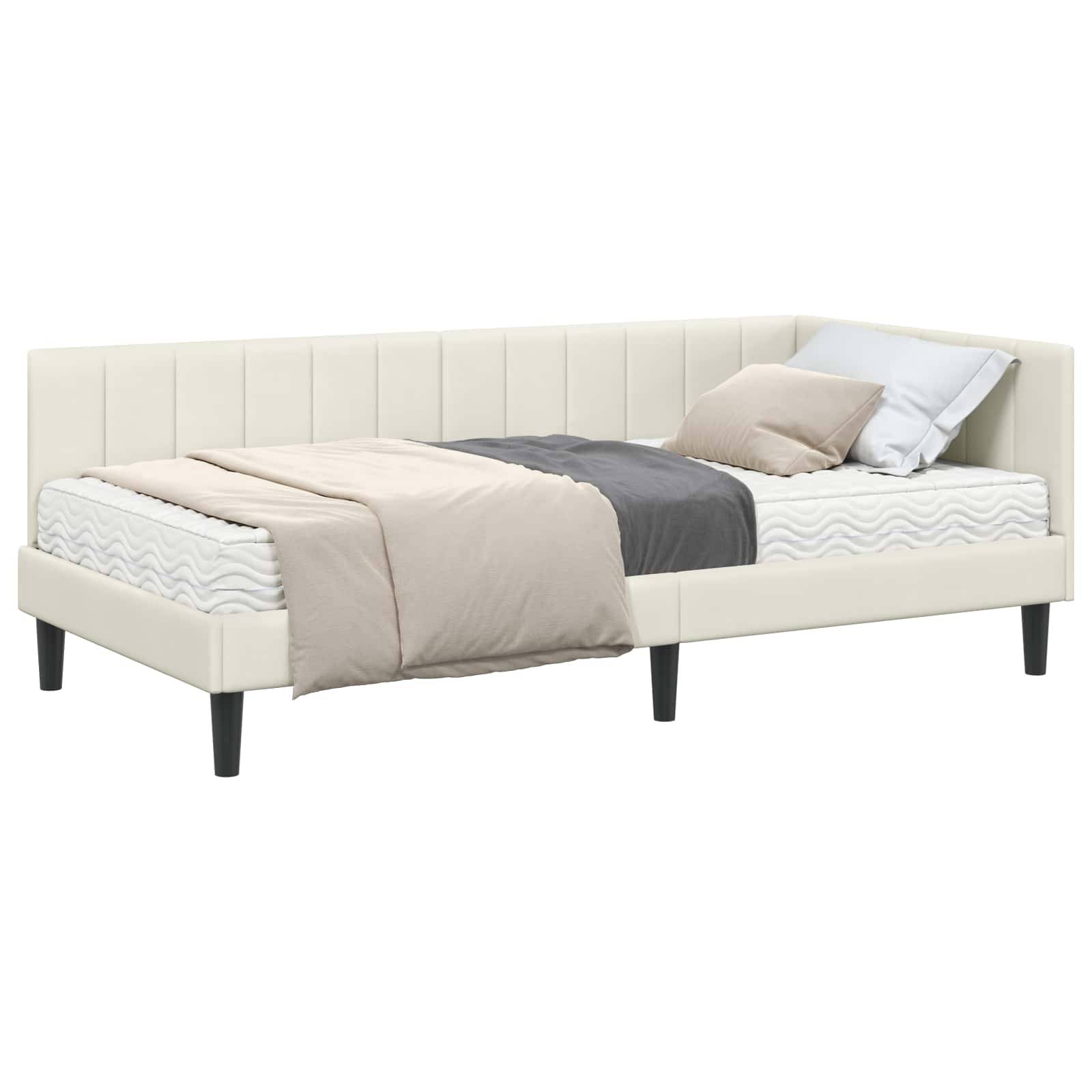 Ein beige gepolstertes Tagesbett mit einer weißen Matratze, hell- und beigefarbener Bettwäsche und einem dunkelgrauen Kissen, auf Holzbeinen stehend.