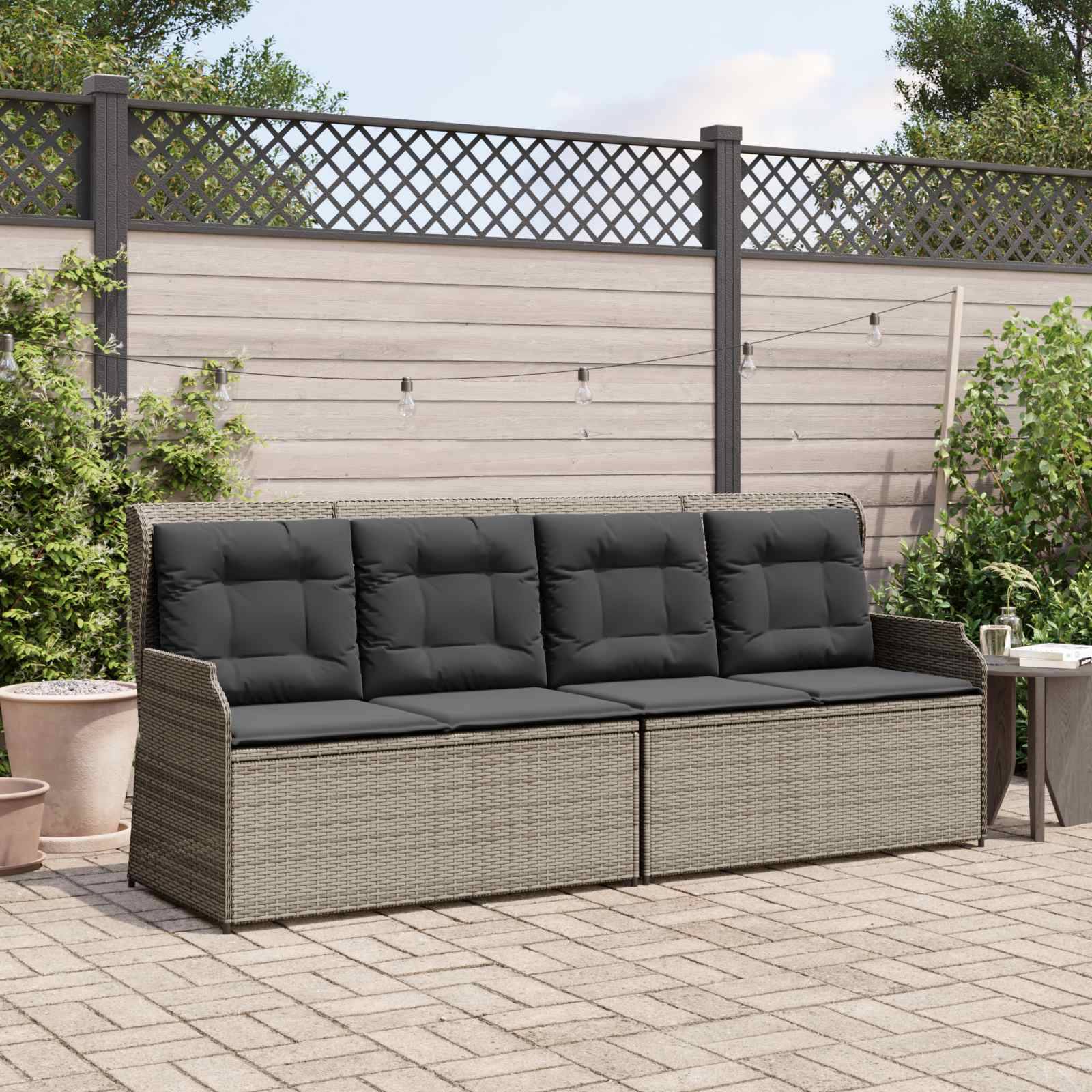 Überdachte Terrasse mit einem Rattansofa, grauen Kissen und Topfpflanzen. Holz-Sichtschutzzaun und ein kleiner runder Tisch mit Glasplatte.