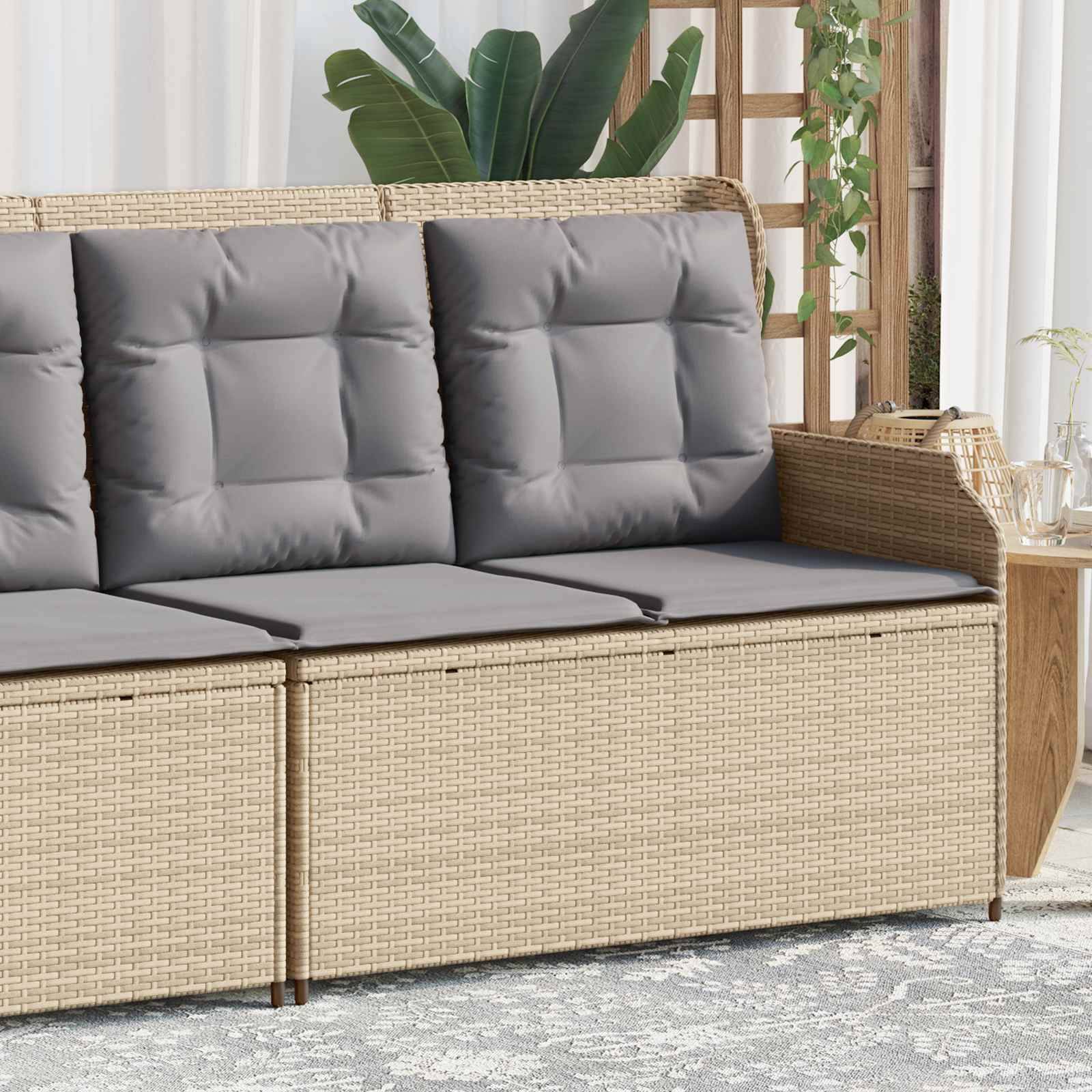Eine beige Rattancouch für den Außenbereich mit dicken grauen Kissen steht auf einem gemusterten Teppich. Grüne Pflanzen und Holzakzente schmücken den Hintergrund.