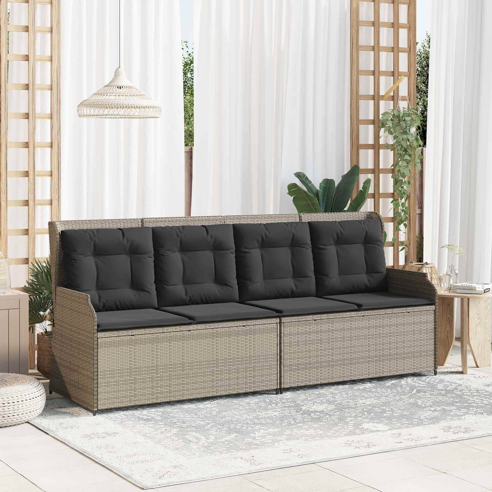 Ein Rattansofa mit schwarzen Kissen steht in einem hellen Außenraum mit weißen Vorhängen, grünen Pflanzen und einem Teppich auf dem Boden.