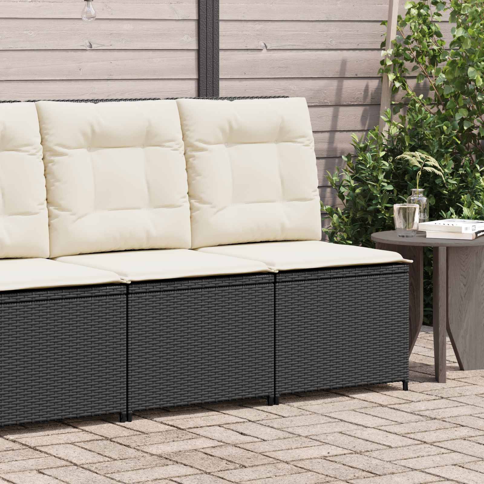Außenterrasse mit einem dreisitzigen gepolsterten Sofa im Rattandesign, daneben ein kleiner runder Tisch mit einem Glas und einer Pflanze. Üppiges Grün im Hintergrund.