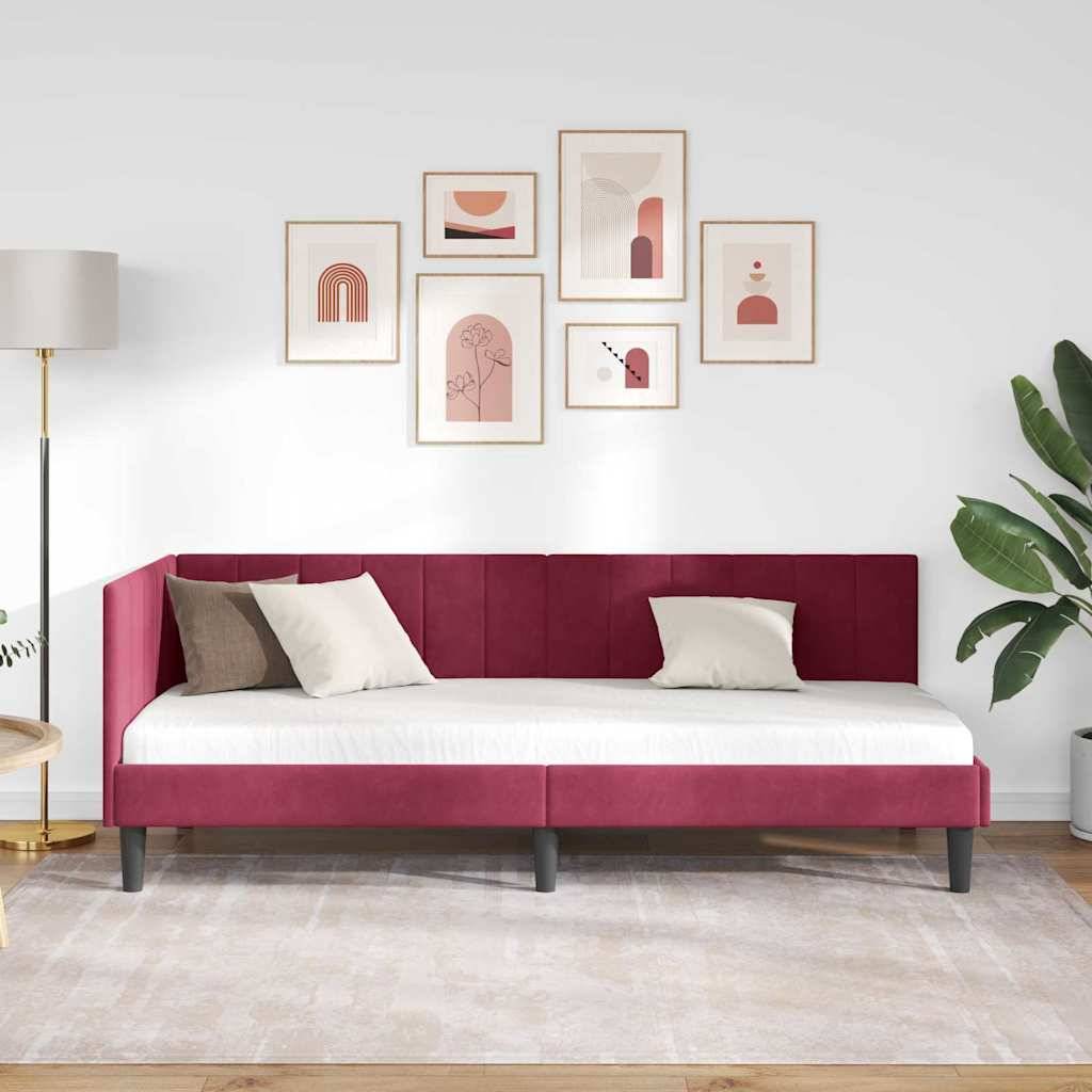 Ein Tagesbett mit bordeauxrotem Polsterbezug und weißer Bettwäsche sowie Kissen steht an einer weißen Wand, darüber abstrakte Wandkunst, mit einer Stehleuchte und einer großen Pflanze in der Nähe.