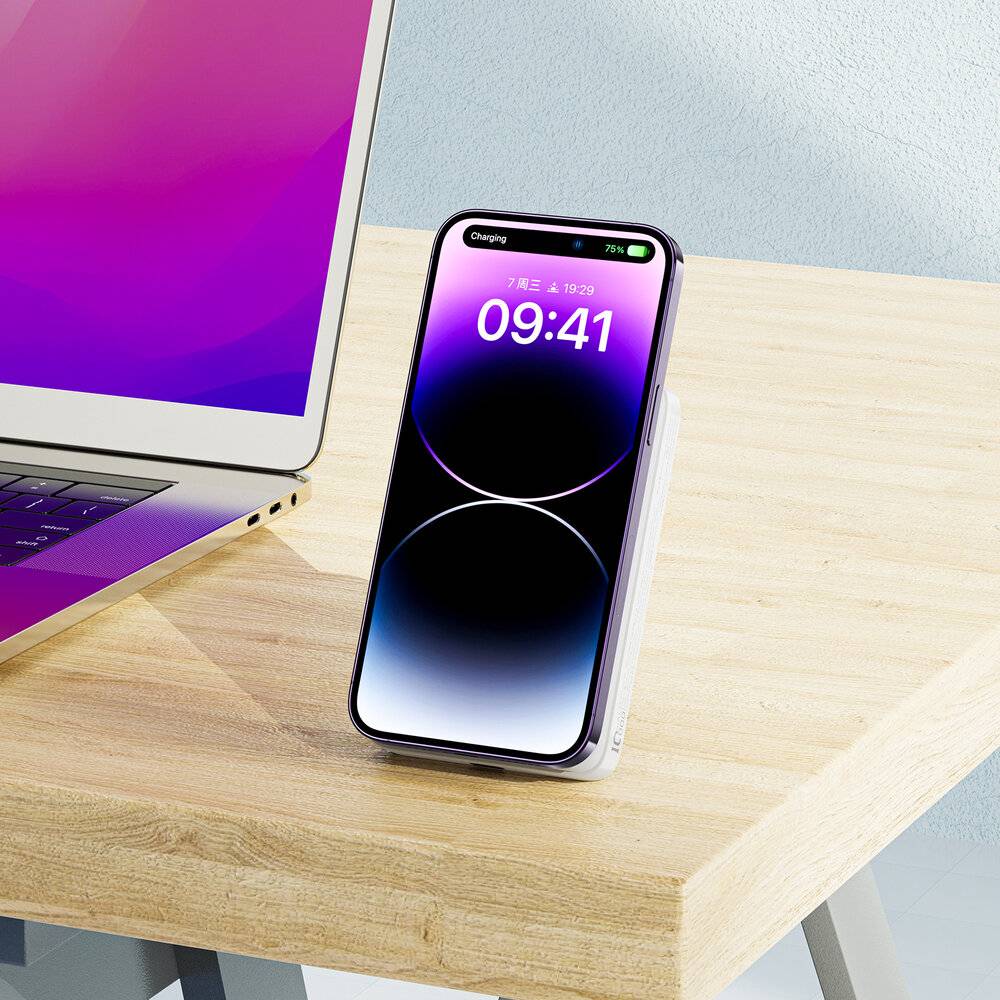 Ein Smartphone auf einer kabellosen Ladestation zeigt die Uhrzeit '09:41' und ein Batteriesymbol, das den Ladevorgang anzeigt. Daneben befindet sich ein offener Laptop.