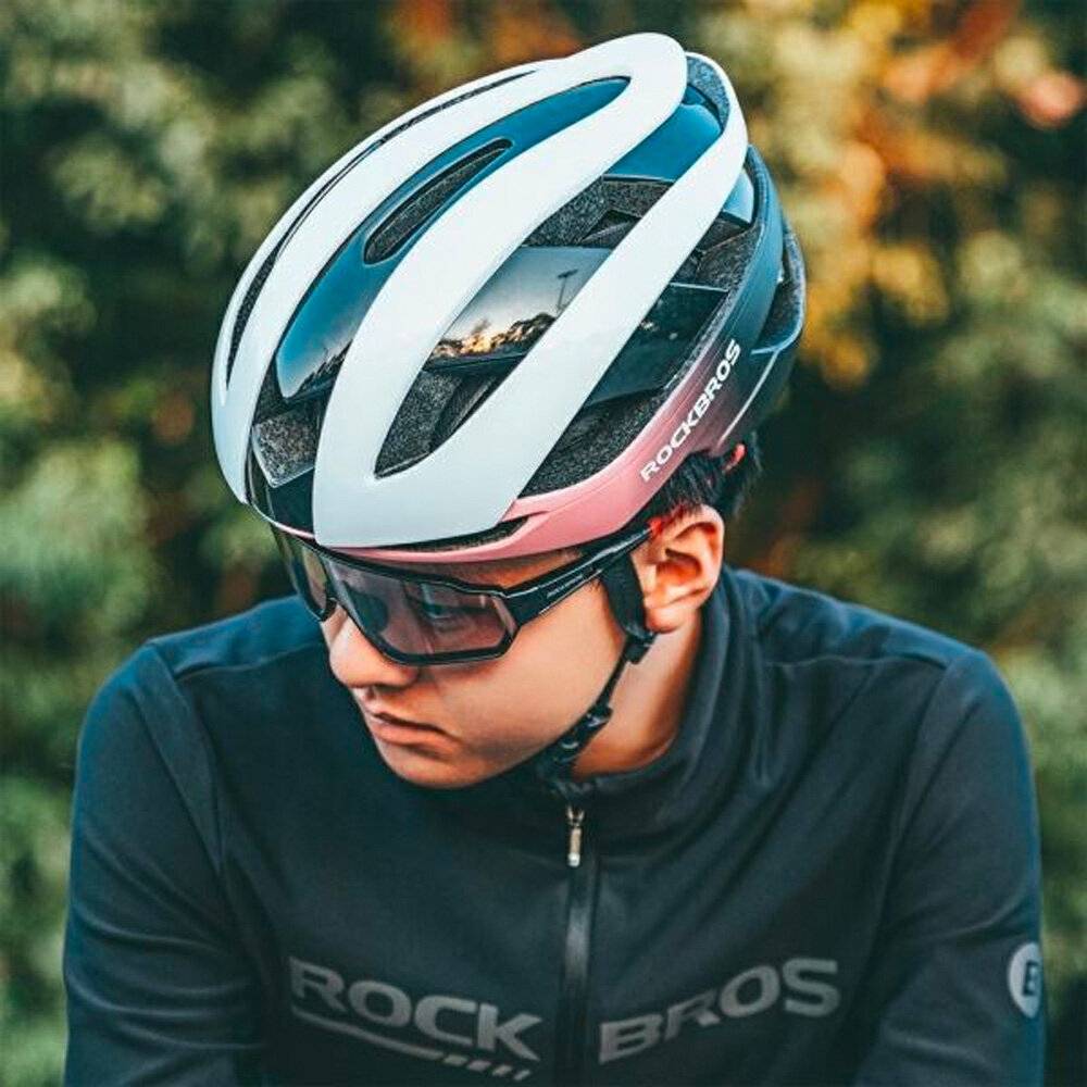 Eine Person, die einen Fahrradhelm und eine Sportsonnenbrille trägt, blickt nach unten, vor einem unscharfen natürlichen Hintergrund.