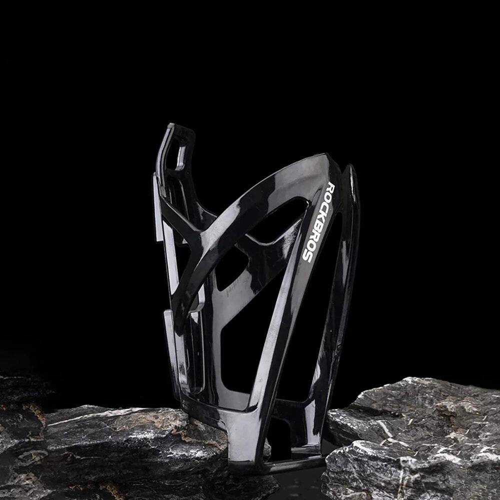 Ein schlanker schwarzer Fahrrad-Flaschenhalter steht aufrecht auf einer rauen Steinoberfläche, wobei der Markenname auf seiner Seite sichtbar ist.