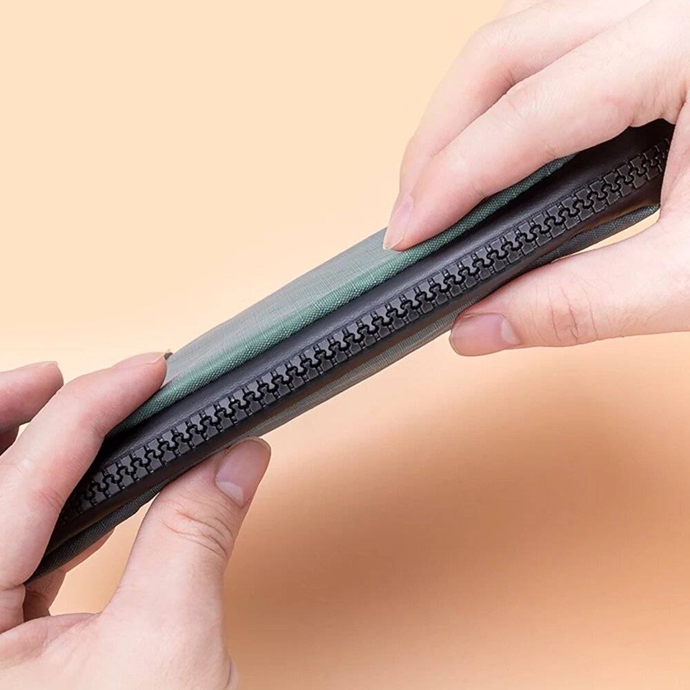 Hände halten eine geschlossene grüne Geldbörse vor einem pfirsichfarbenen Hintergrund.