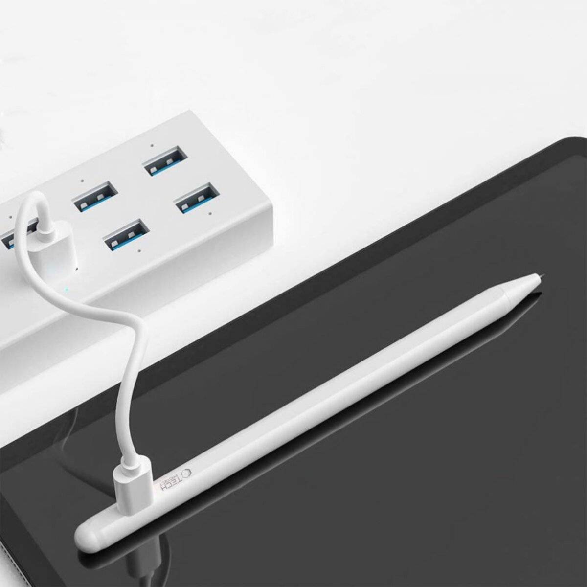 Ein weißer Stylus lädt über ein USB-Kabel, das mit einem USB-Hub verbunden ist. Der Hub verfügt über mehrere USB-Anschlüsse und befindet sich neben einem Tablet-Bildschirm.