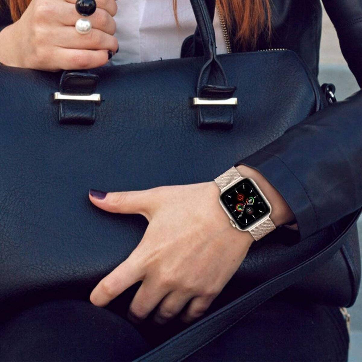 Eine sitzende Person, die eine schwarze Handtasche mit einer Hand hält und eine Smartwatch am Handgelenk trägt. Der Fokus liegt auf der Uhr und der Handtasche.