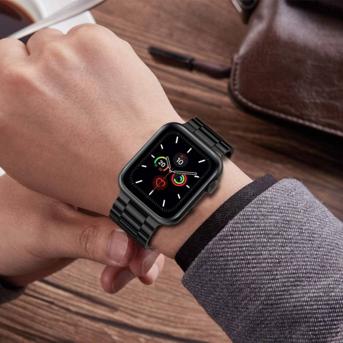 Eine Person mit einer Smartwatch, die Fitnessverfolgungsdaten anzeigt, mit einer Kaffeetasse und einem Ledernotizblock im Hintergrund auf einem Holztisch.