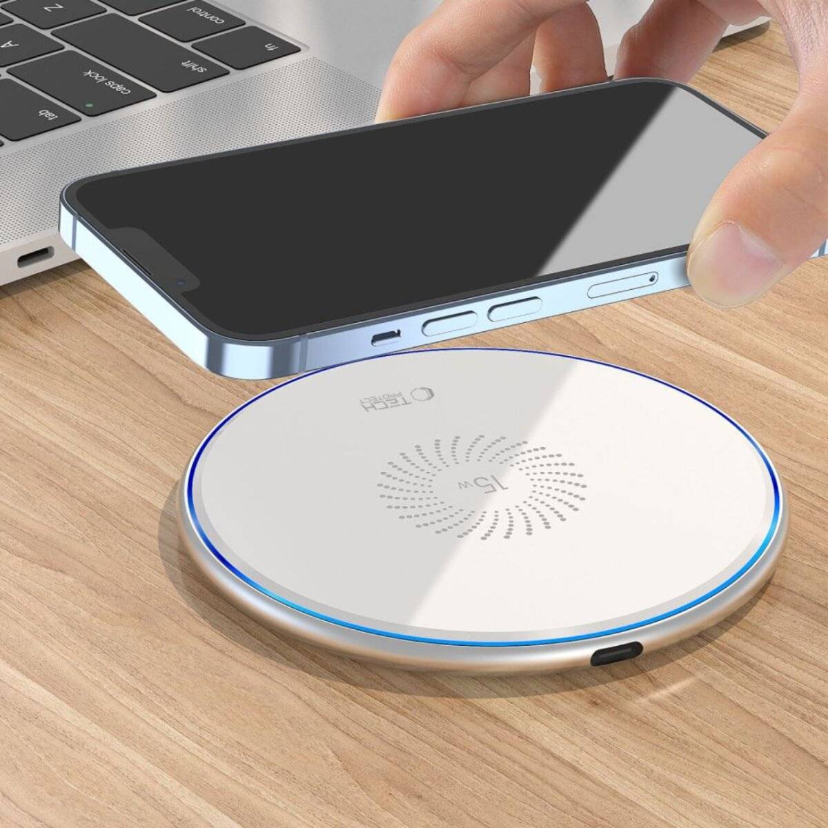 Eine Hand legt ein Smartphone auf ein weißes drahtloses Ladegerät, das auf einem Holztisch neben einer Laptop-Tastatur liegt.