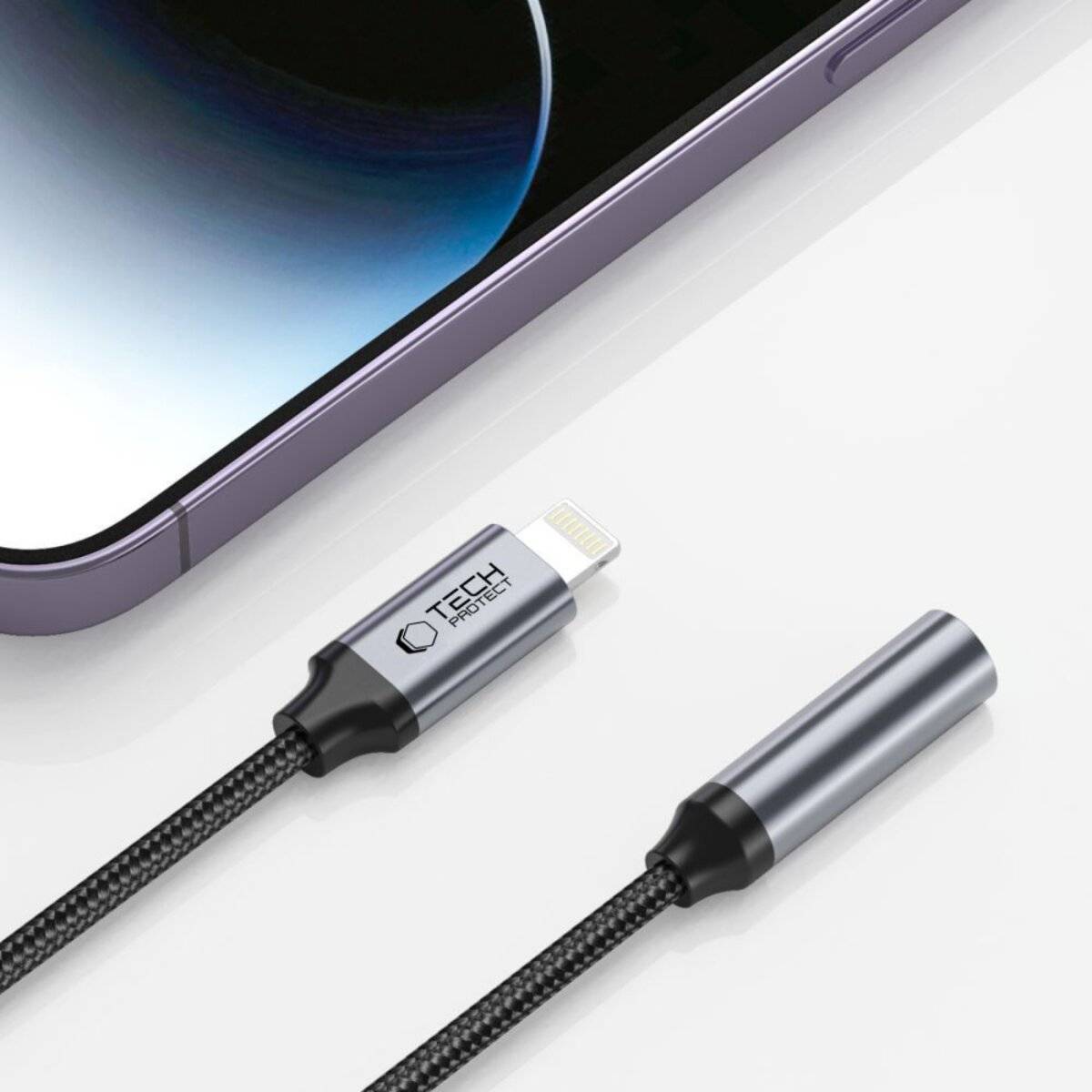 Eine Nahaufnahme der Ecke eines Smartphones und zwei schwarze Ladekabel mit Metallsteckern auf einer weißen Oberfläche.