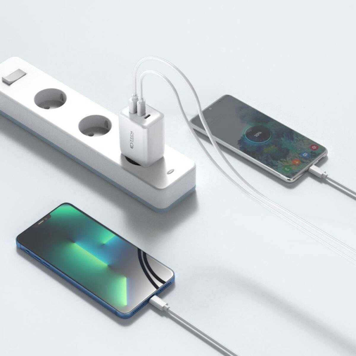 Zwei Smartphones laden: eines kabellos auf einer Ladestation, ein anderes über ein Kabel verbunden mit einer Steckerleiste mit mehreren Steckdosen.