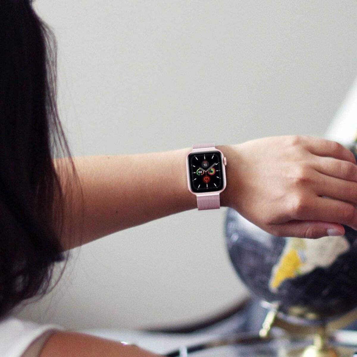 Eine Person mit einer Smartwatch überprüft die Uhrzeit. Das Zifferblatt zeigt verschiedene Symbole, und das Armband ist in einer hellen Farbe gehalten.