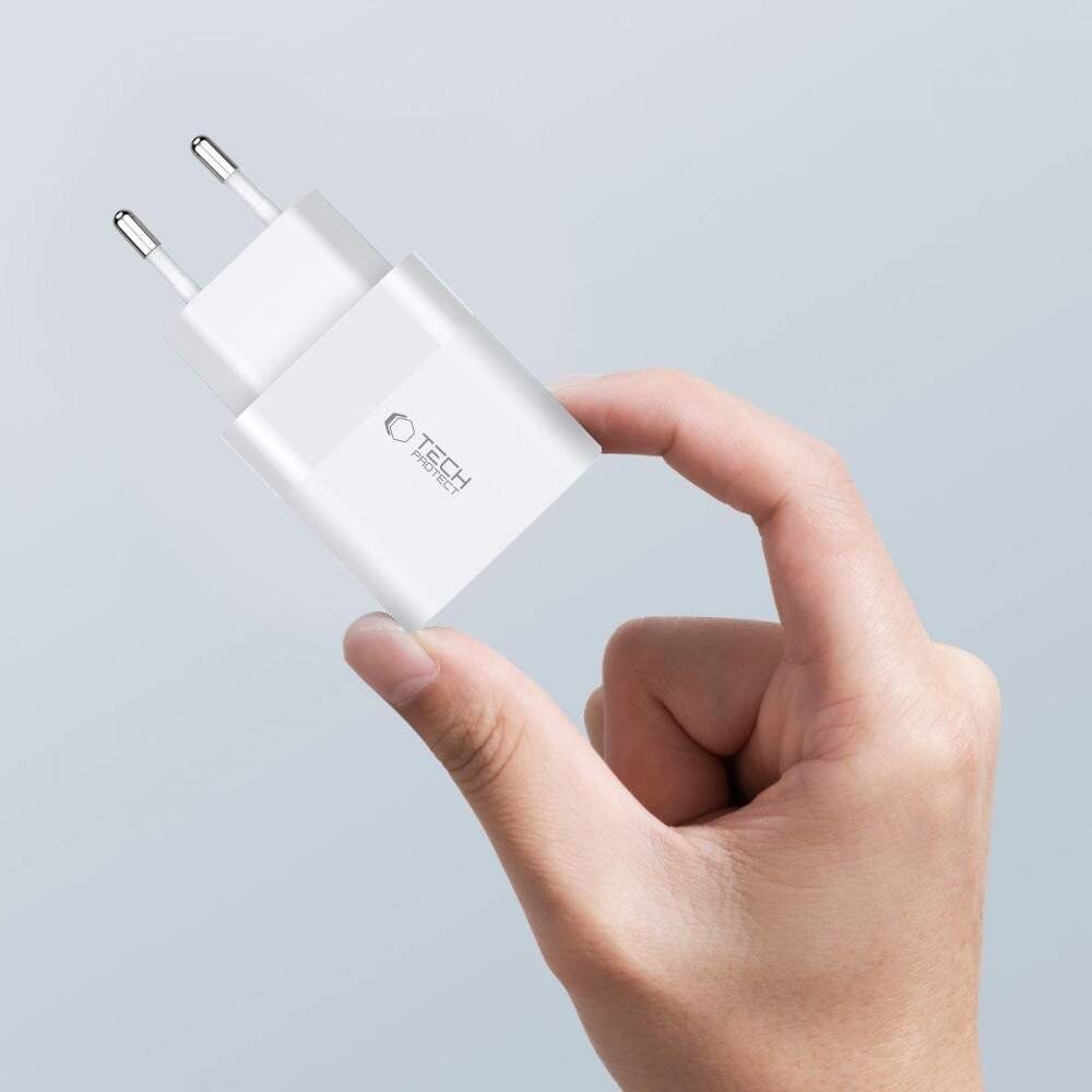 Eine Hand hält einen weißen Stromadapter mit europäischem Stecker, auf dem das „Tech