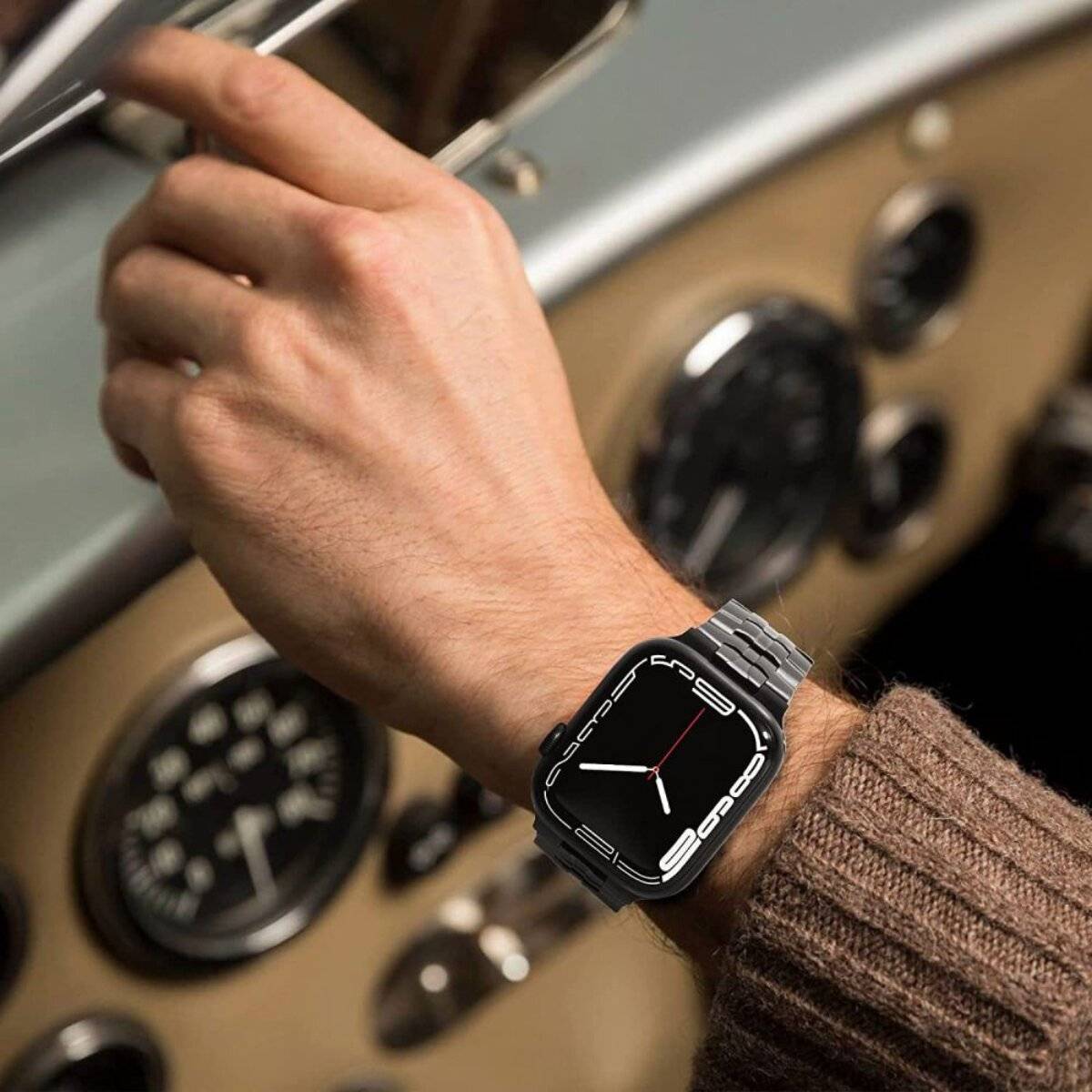 Eine Person, die eine Smartwatch mit einem eleganten, metallischen Armband trägt, ist vor einem alten Armaturenbrett eines Autos mit mehreren Ziffernblättern zu sehen.