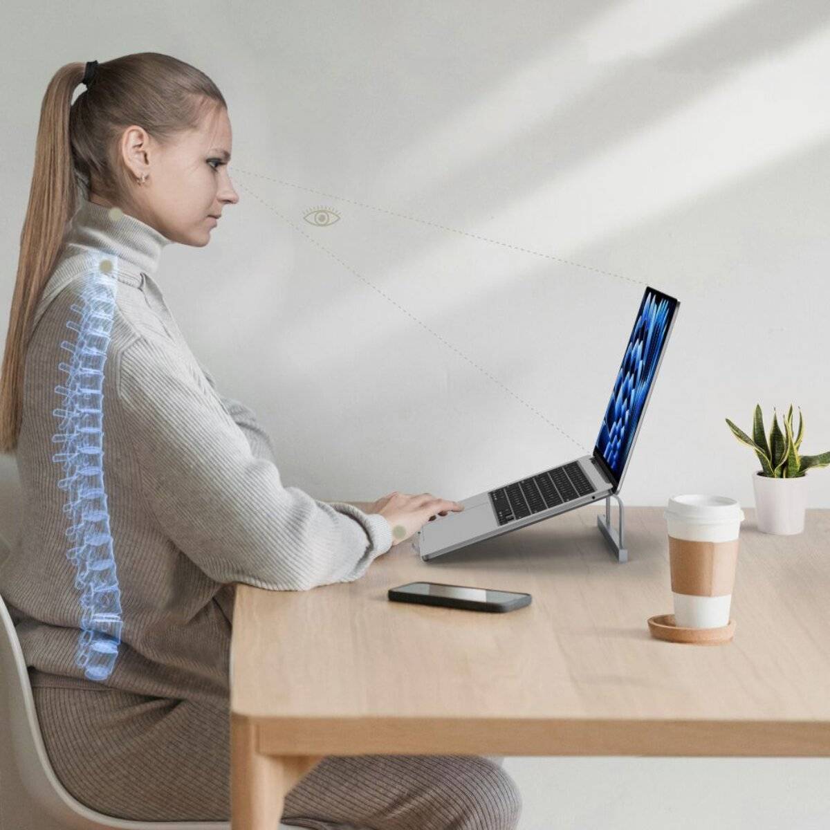 Eine Frau nutzt einen Laptop an einem Schreibtisch und behält dabei eine ergonomische Körperhaltung bei. Ein Telefon und eine Kaffeetasse befinden sich in der Nähe; eine Pflanze schmückt den Raum.