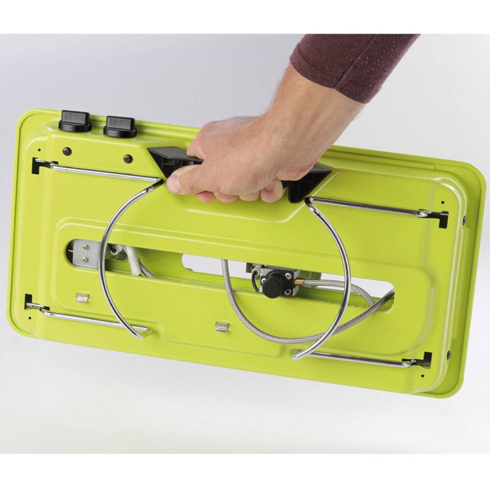 Eine Person hält einen grünen, tragbaren Gaskocher verkehrt herum, um dessen Unterseite zu zeigen, mit sichtbaren Metallstützen und Bedienknöpfen.