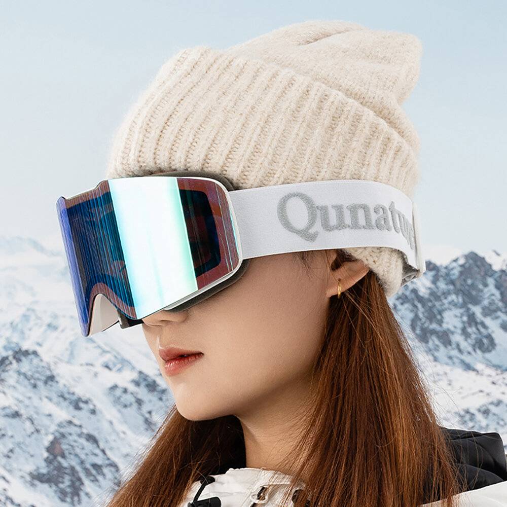 Person trägt reflektierende Skibrillen und eine Strickmütze und steht vor einer verschneiten Bergkulisse.