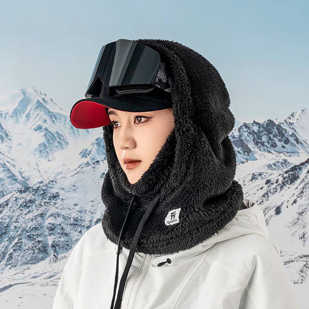 Eine Person in Winterkleidung, einschließlich einer schwarzen Kapuze und Sonnenbrille, steht vor schneebedeckten Bergen.