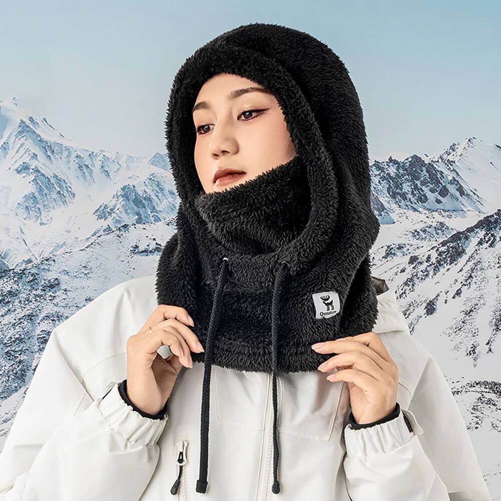 Eine Person in einer weißen Jacke und einem schwarzen Kapuzenschal steht vor einer verschneiten Berglandschaft und schaut nachdenklich.