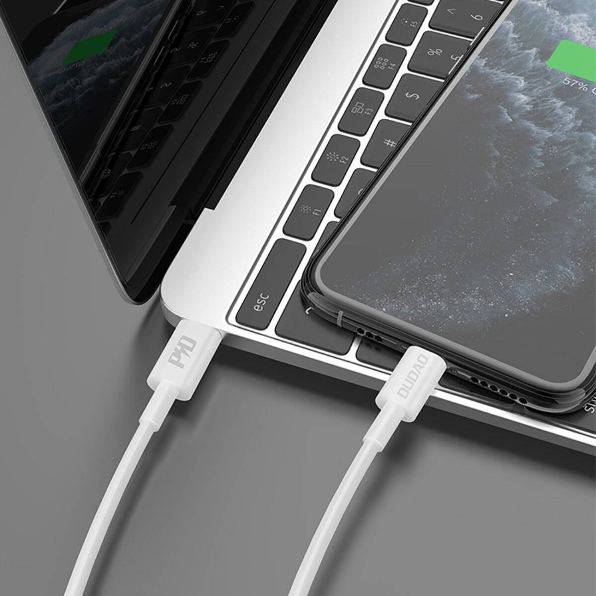 Ein Laptop, der ein Smartphone über ein weißes Kabel lädt, wobei beide Geräte auf einem Schreibtisch zu sehen sind und der Bildschirm des Telefons ein Batteriesymbol zeigt.