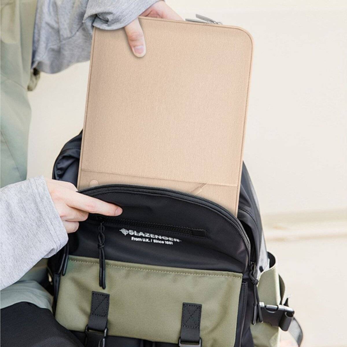 Eine Person legt ein Tablet in einen grün-schwarzen Rucksack mit externen Taschen, was auf Reisevorbereitungen oder Lernvorbereitung hindeutet.