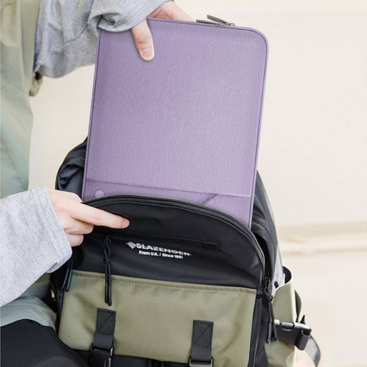Eine Person legt ein lila Tabletthülle in die Vordertasche eines zweifarbigen Rucksacks und hebt dabei die praktische Aufbewahrung und die leichte Zugänglichkeit hervor.