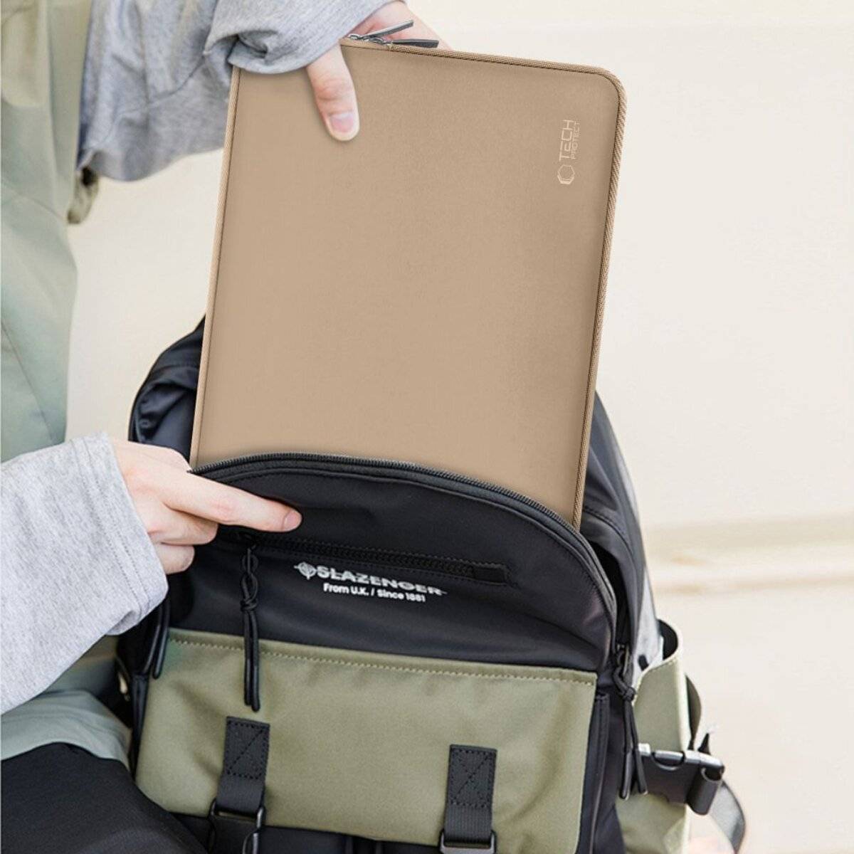 Eine Person legt ein beiges Tablet in einen kleinen schwarz-grünen Rucksack.