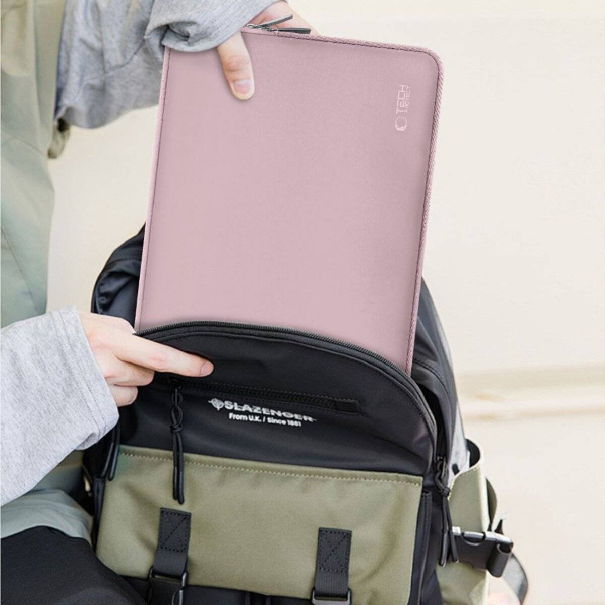 Eine Person, die einen E-Reader mit rosa Umschlag hält und ihn in einen grau-schwarzen Rucksack legt.
