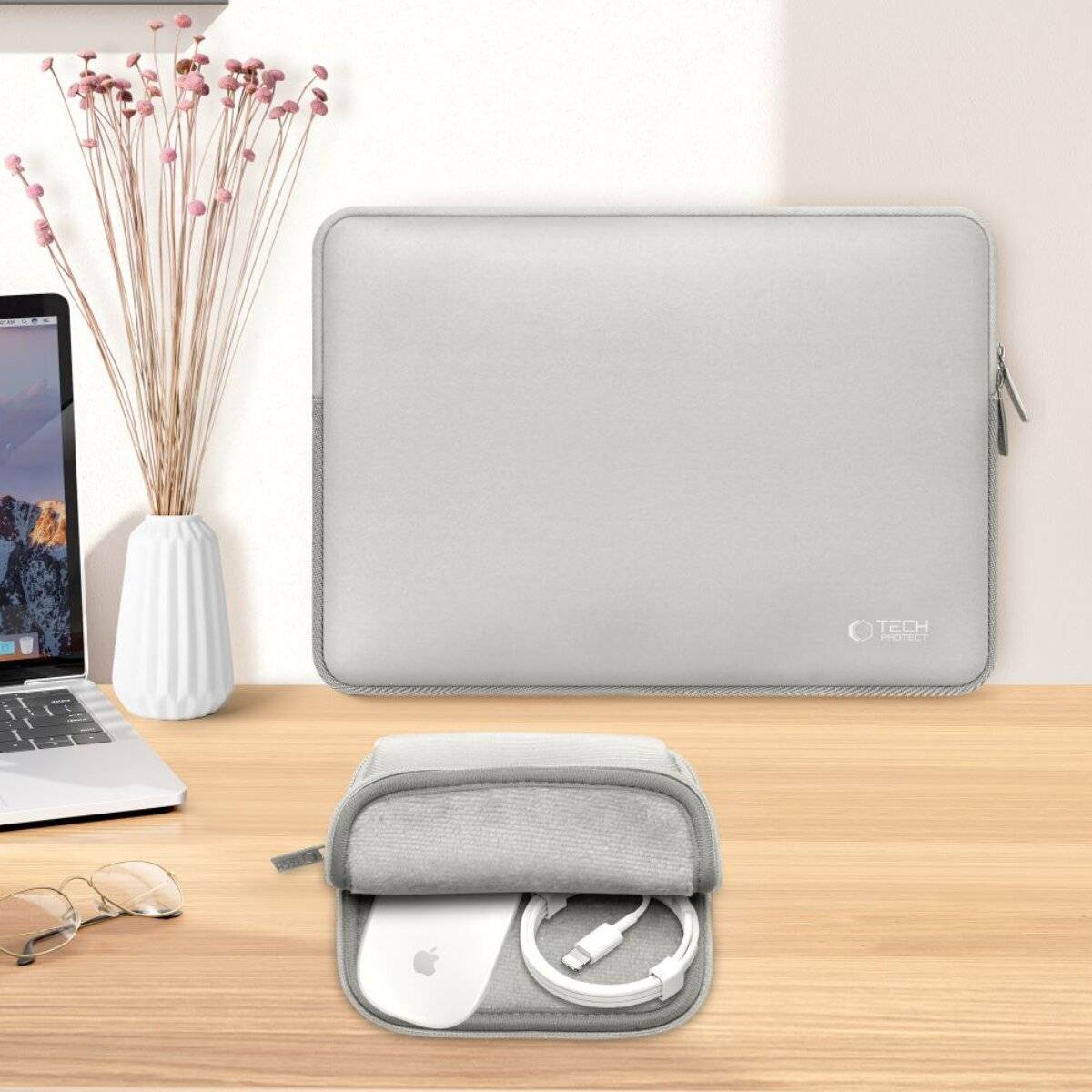 Ein Laptop-Schutzhülle und eine Zubehörtasche auf einem Holzschreibtisch. Die Hülle ist weiß mit einem Reißverschluss und befindet sich neben einem Laptop und einer kleinen Vase.