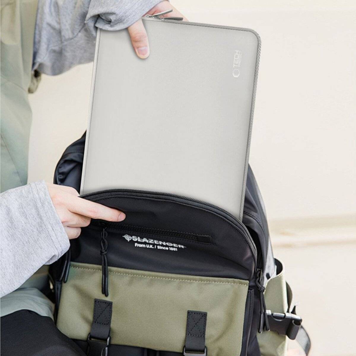 Eine Person, die ein graues Tablet in einen schwarz-grünen Rucksack legt, wobei das Tablet teilweise sichtbar ist.