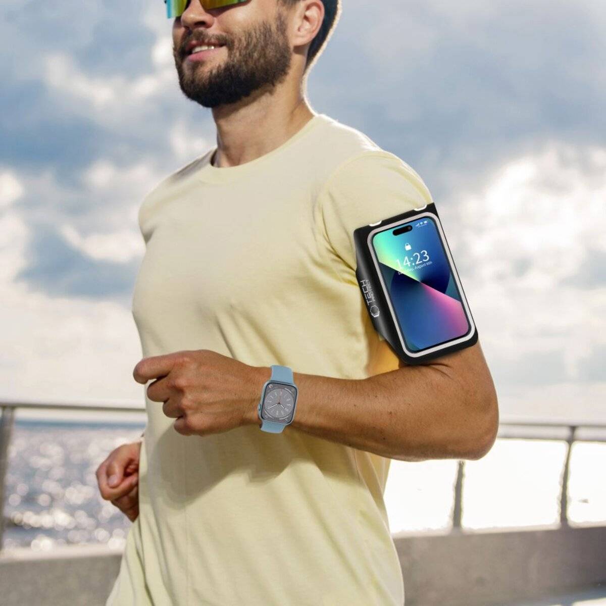 Mann joggt am Meer und trägt eine Smartwatch und eine Smartphone-Armbinde.