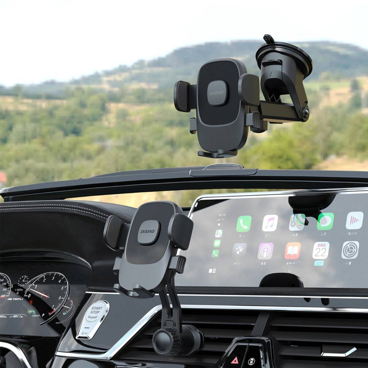 Das Bild zeigt ein Armaturenbrett eines Autos mit zwei Handyhalterungen, die eine ländliche Landschaft durch die Windschutzscheibe hindurch sichtbar machen.