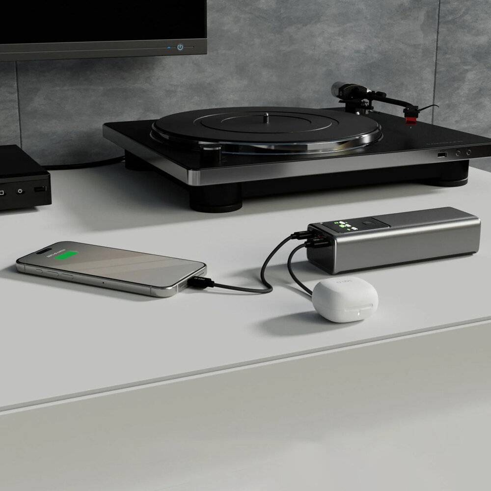 Ein Smartphone wird auf einem Tisch mit einer Powerbank aufgeladen. In der Nähe befindet sich ein moderner Plattenspieler, was eine Mischung aus Technologie andeutet.