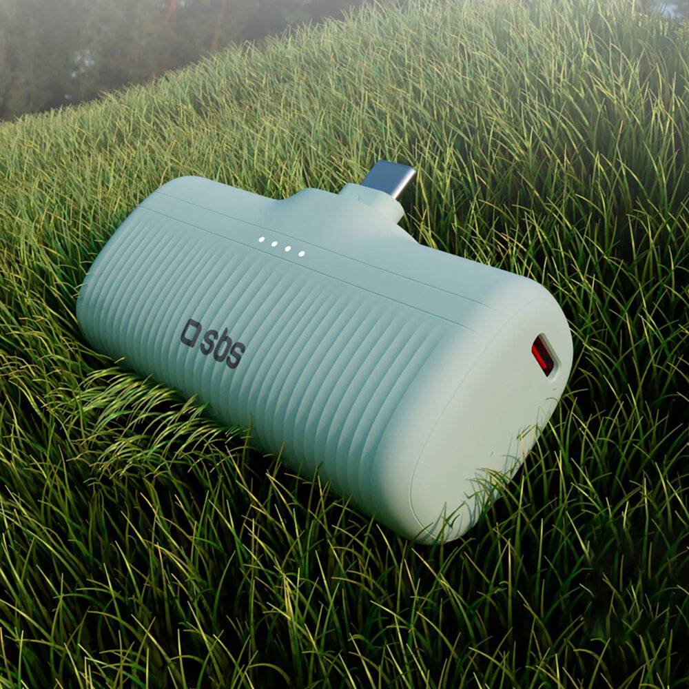Ein tragbarer Lautsprecher mit 'sbs'-Branding ruht auf einer üppigen Grasfläche, beleuchtet durch weiches natürliches Umgebungslicht.