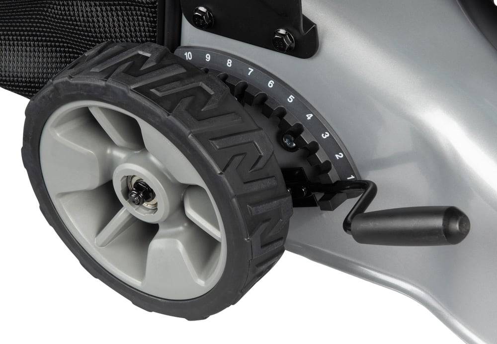 Nahaufnahme eines Rasenmäherrades neben einem Höhenverstellhebel mit einer Skala von 1 bis 10, die verschiedene Schnitthoheoptionen anzeigt.