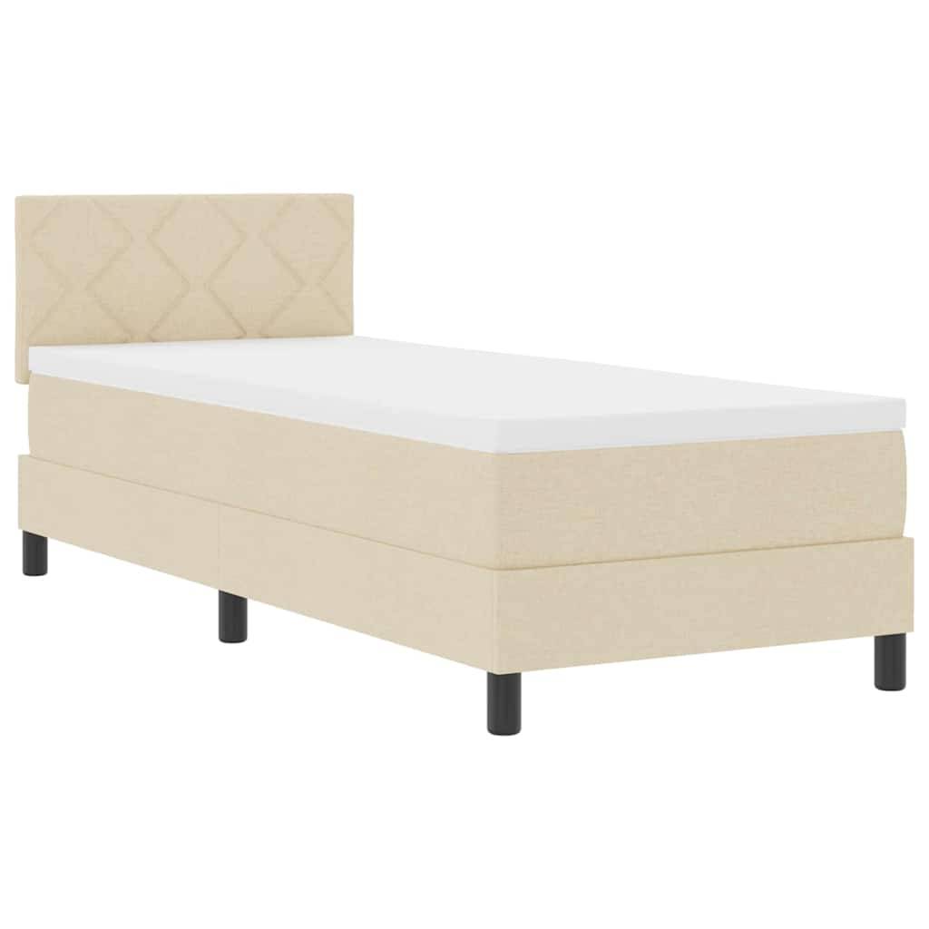 Ein beige farbenes Einzelbett mit einem rauten-gemusterten Kopfteil und schwarzen Beinen vor einem schlichten weißen Hintergrund.