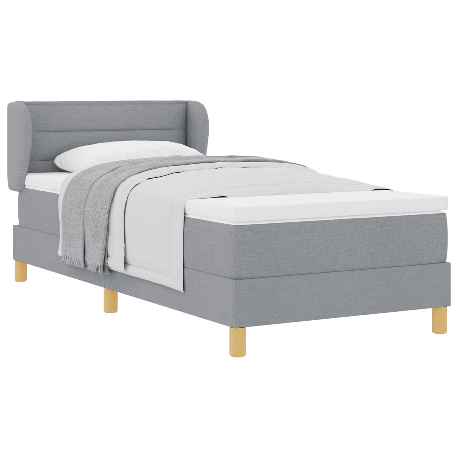 Grau gepolstertes Einzelbett mit weißer Bettwäsche und einer Decke, gezeigt auf weißem Hintergrund.