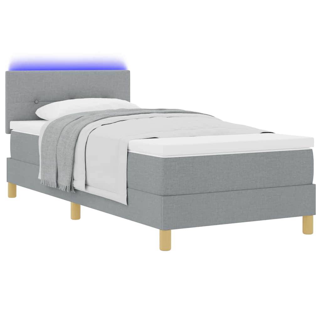 Grau gepolstertes Einzelbett mit weißer Bettwäsche und einer leuchtenden blauen Kopfleuchte auf weißem Hintergrund.