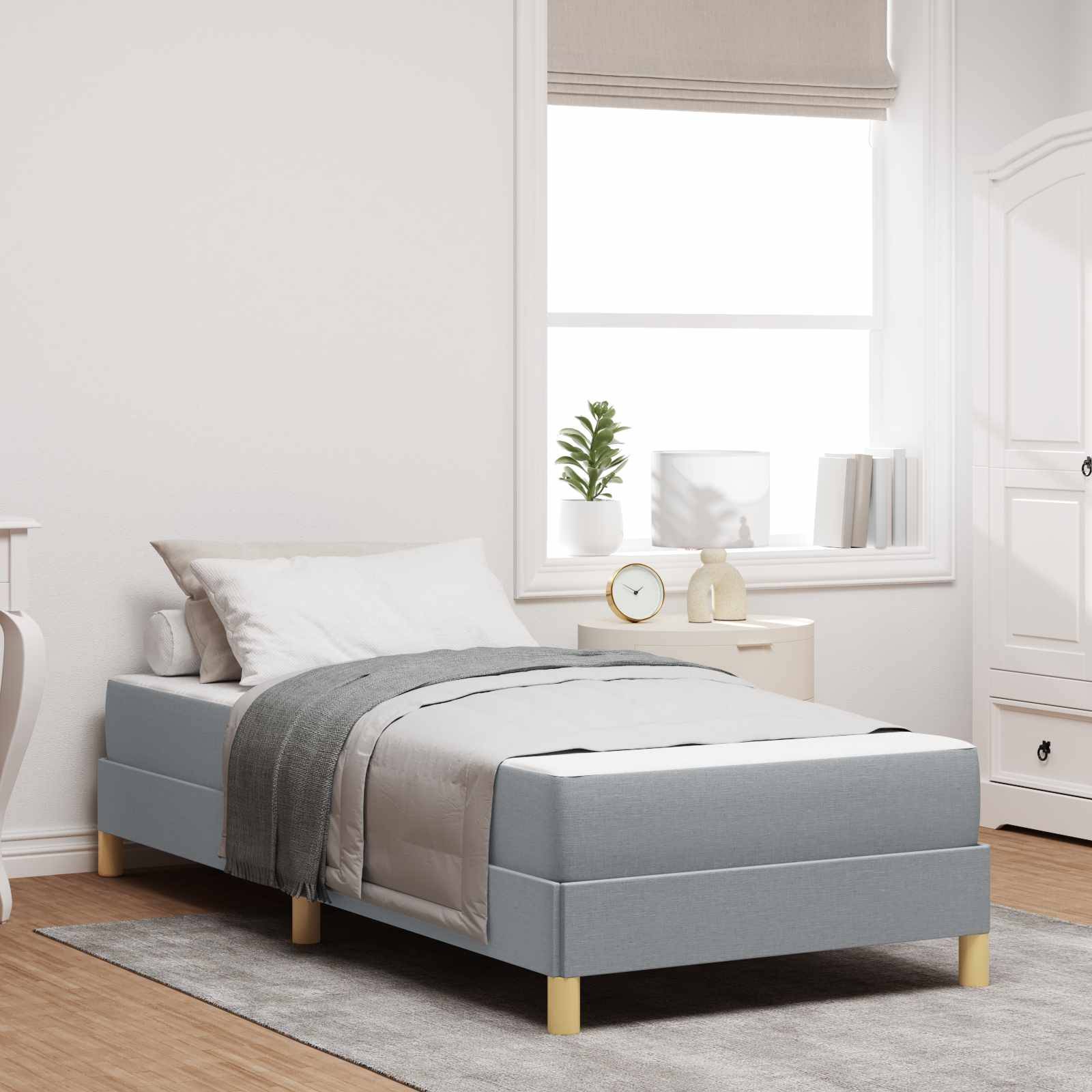 Minimales Schlafzimmer mit einem Einzelbett, grauer Bettwäsche, einem Nachttisch am Fenster und einem weißen Kleiderschrank auf einem hellen Teppich und Holzboden.