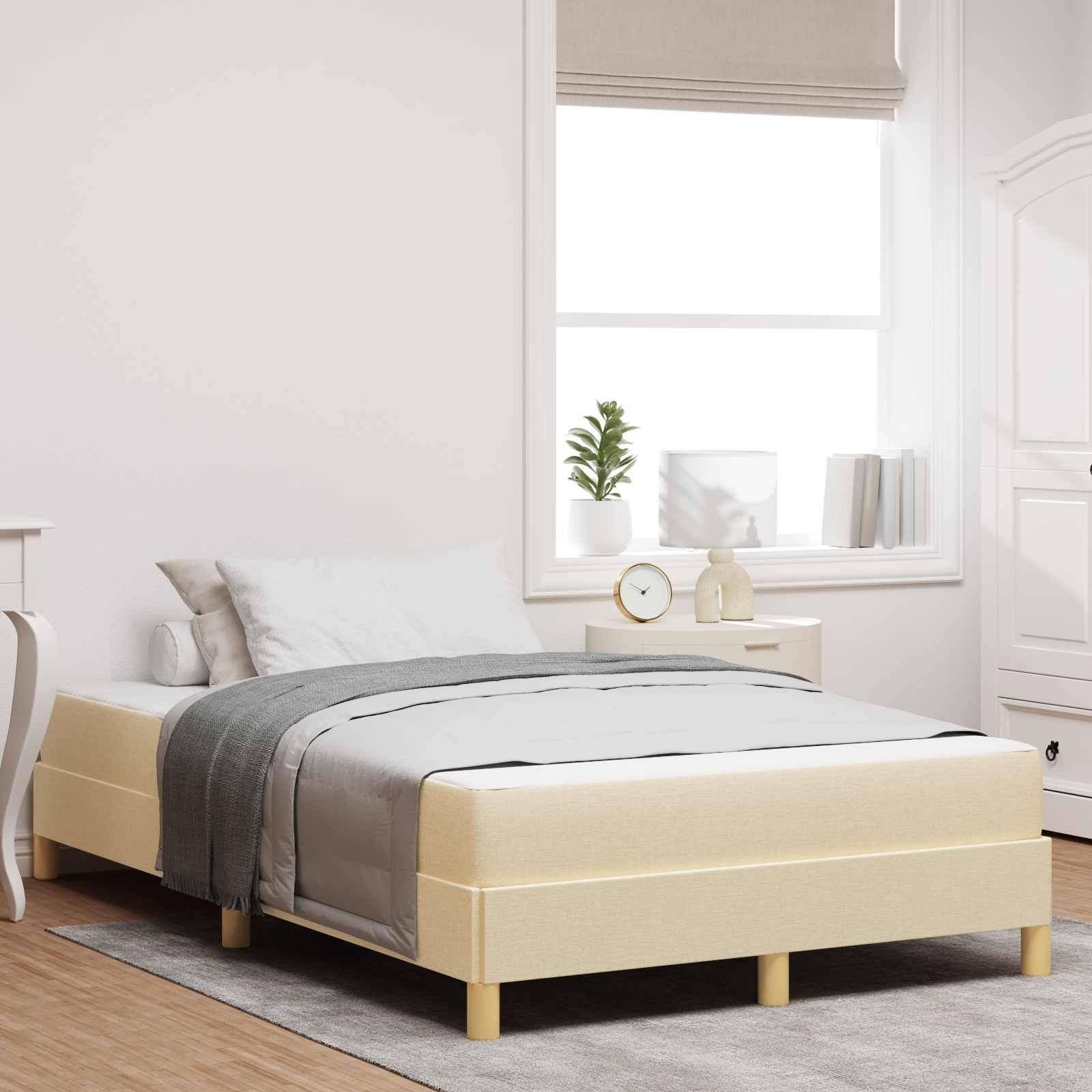 Ein ordentlich gemachtes Bett mit grauer Bettwäsche in einem hellen Raum mit Fenster, Pflanzen, Lampe und Büchern, das eine ruhige und aufgeräumte Atmosphäre schafft.