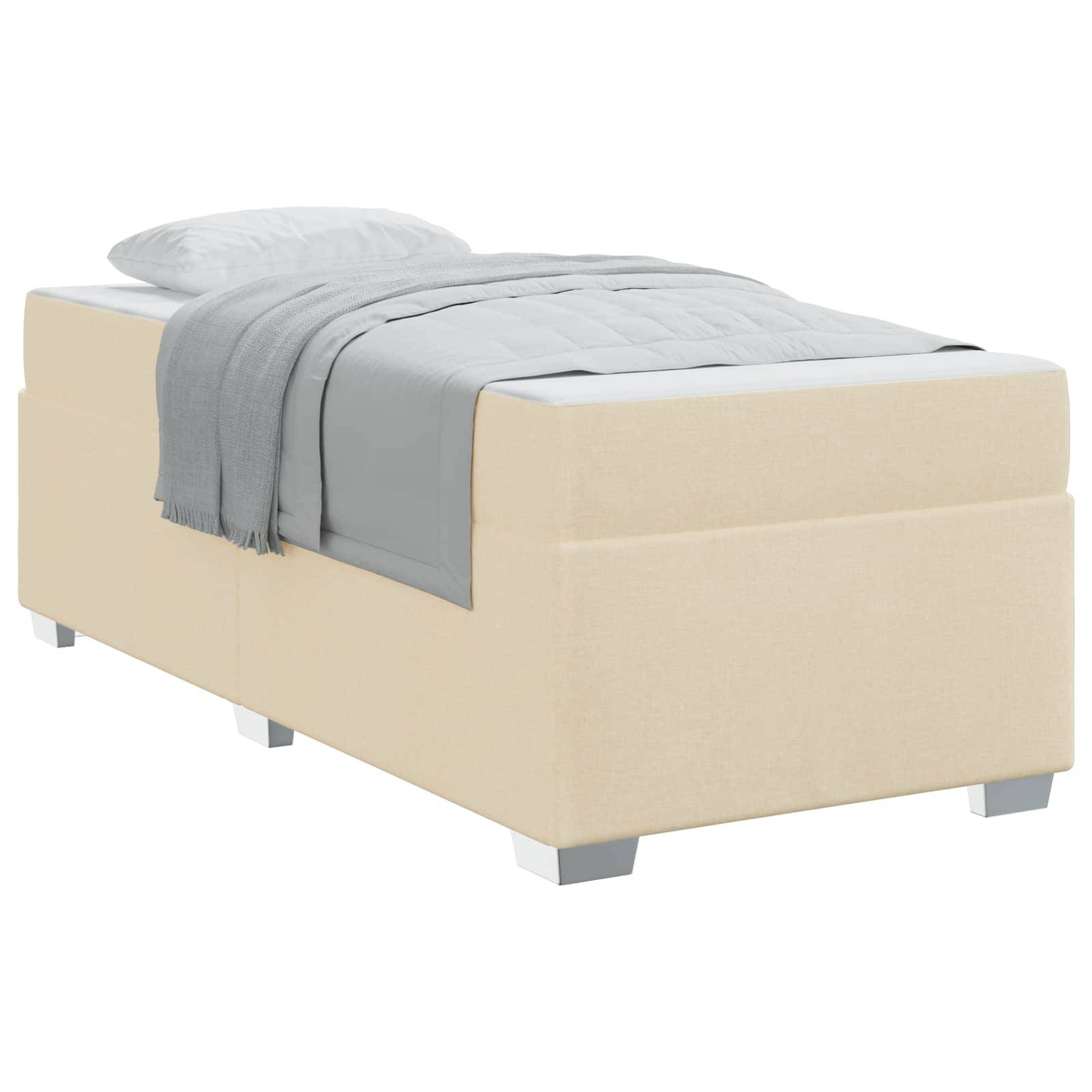 Ein beiges Einzelbett mit einem weißen Kissen und einer grau drapierte Decke, die ordentlich darüber liegt.