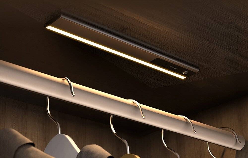 Ein elegantes, modernes LED-Streifenlicht, das unter einem Holzschrank installiert ist und eine Kleiderstange darunter mit weichem, warmem Licht beleuchtet.