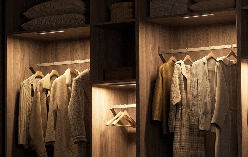 Ein gut organisierter Holzschrank mit hängenden Mänteln und Pullovern, beleuchtet durch Deckenleuchten, mit ordentlich gefalteten Handtüchern auf dem obersten Regal.