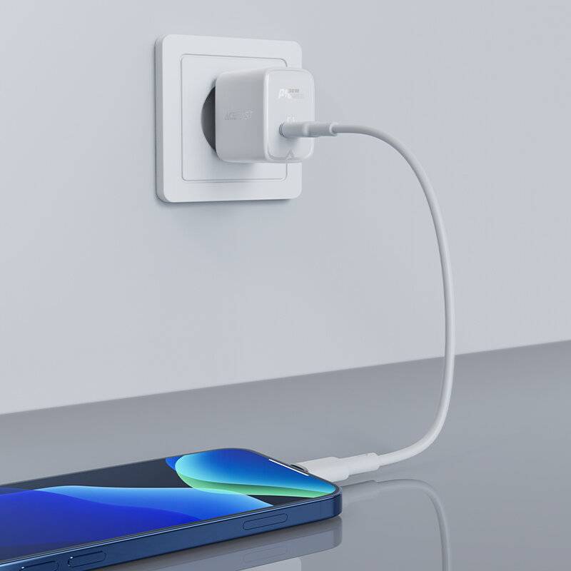 Ein Smartphone mit einem blau-grünen Bildschirm wird auf einer reflektierenden grauen Oberfläche aufgeladen. Ein weißes Kabel verbindet es mit einem Wandsteckeradapter.
