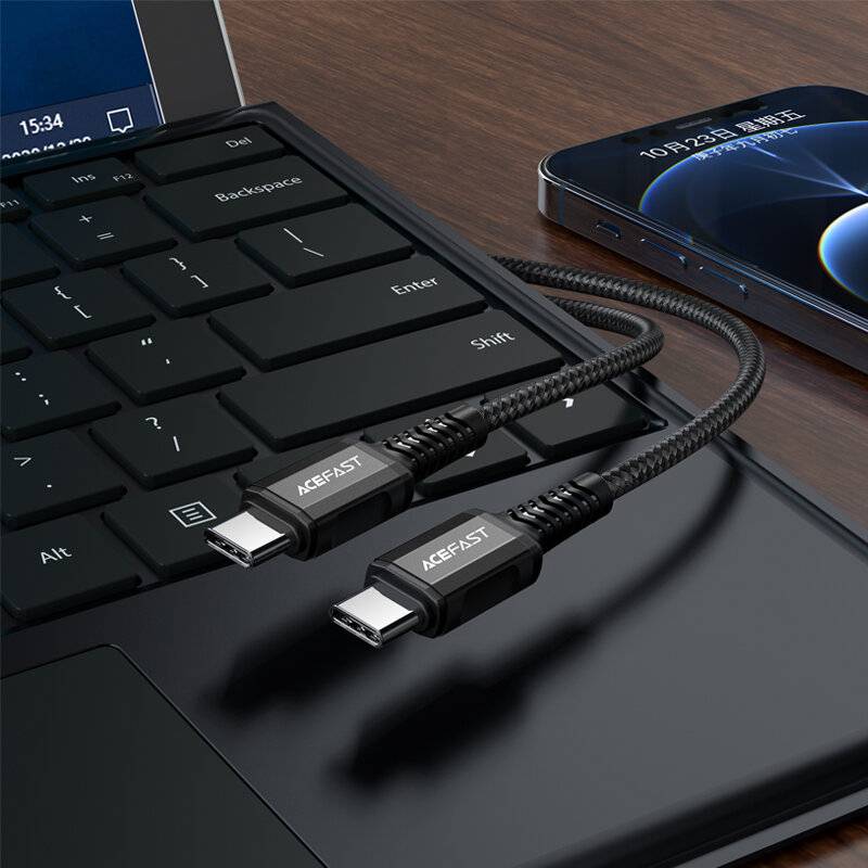 Zwei schwarze ACEFAST USB-C-Kabel, die mit einem Laptop verbunden sind, mit einem Smartphone daneben auf einer glatten, reflektierenden Oberfläche.