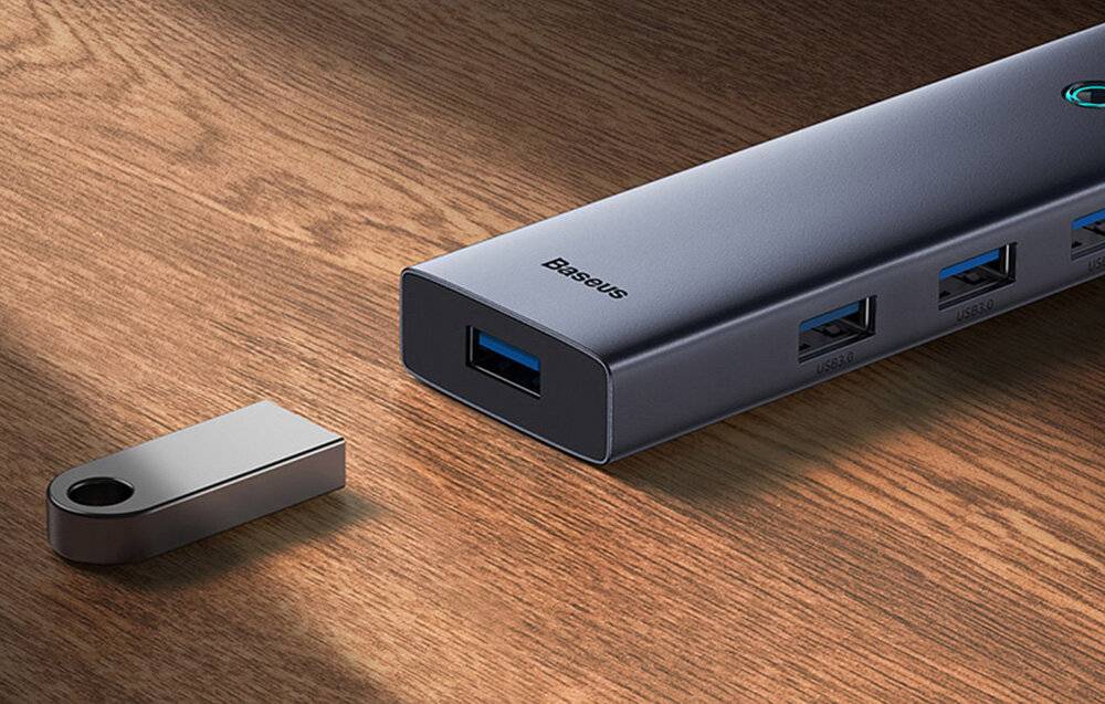 Ein grauer USB-Hub mit mehreren USB-Anschlüssen auf einer Holzoberfläche, mit blauen USB-Steckern und 